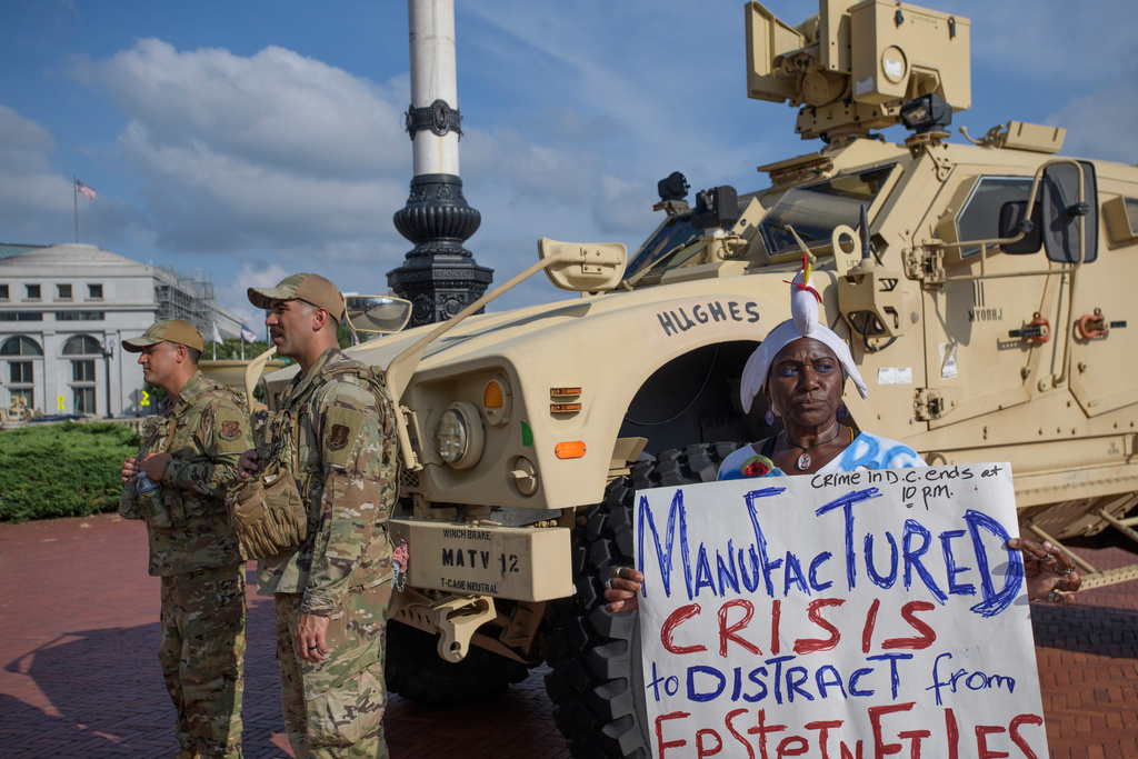 Protester Nadine Seiler holds her sign near National Guard members from the 167th Security Forces from West Virginia, outside Union Station in Washington, Wednesday, Aug. 20, 2025.