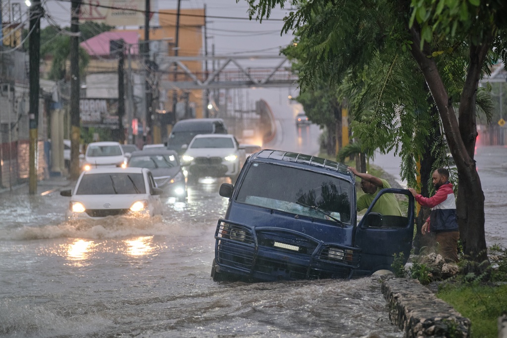 People abandon a car on an impassable street flooded by rains caused by Tropical Storm Melissa in Santo Domingo, Dominican Republic, Friday, Oct. 24, 2025.