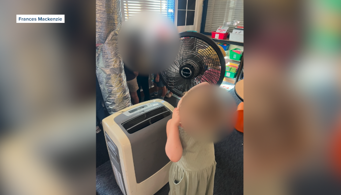 A McKinley Elementary Kindergarten student is seen cooling themselves off next to an AC unit and a fan inside Frances Mackenzie's classroom.