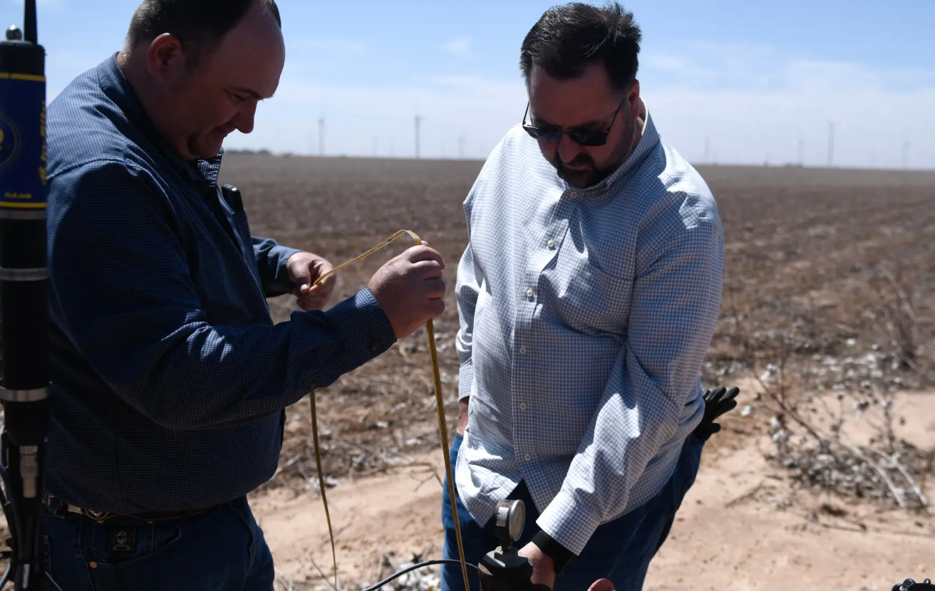 High Plains Underground Water District Field Technician Supervisor Billy Barron, left, and Permit Administrator Gray Sanders measure a well on May 21, outside of Slaton.