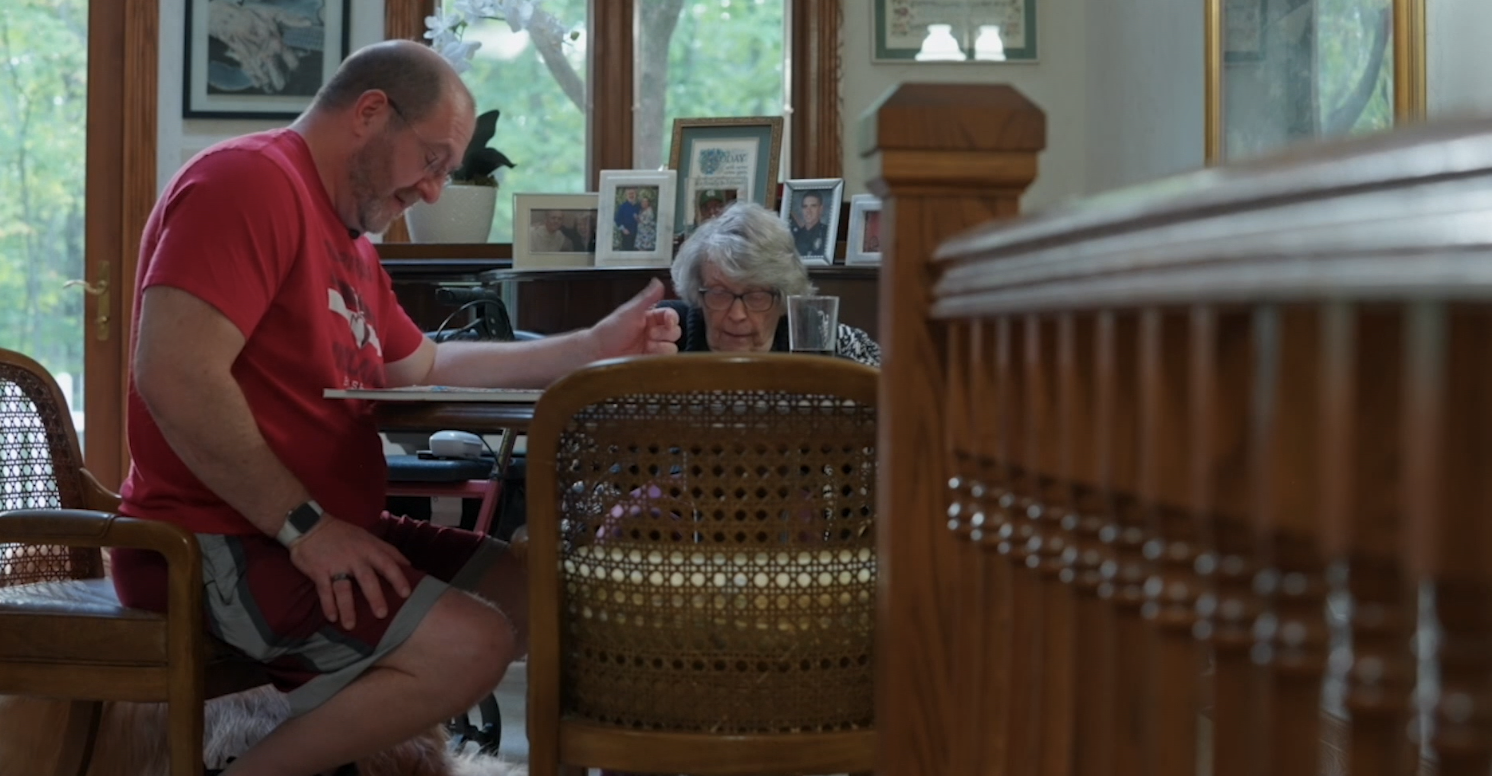 A man sits at a table with his mother. 