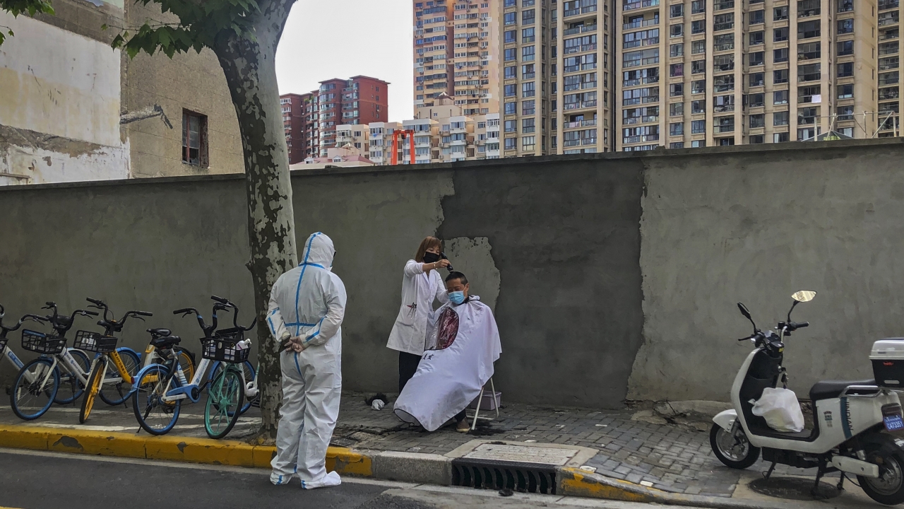 A worker in protective gear watches a barber cut a man's hair on the street in Shanghai.