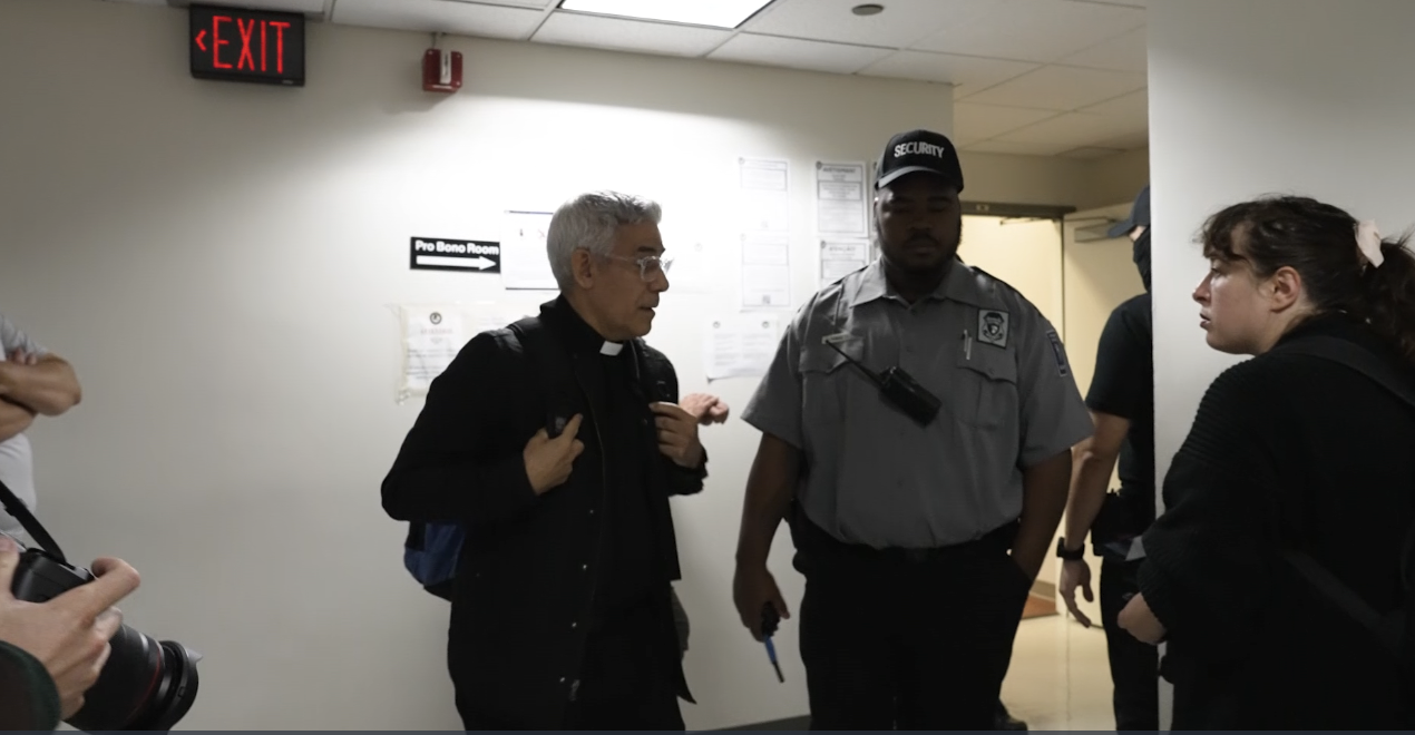 Father Eduardo Fabian Arias is surrounded by security at an ICE courthouse. 