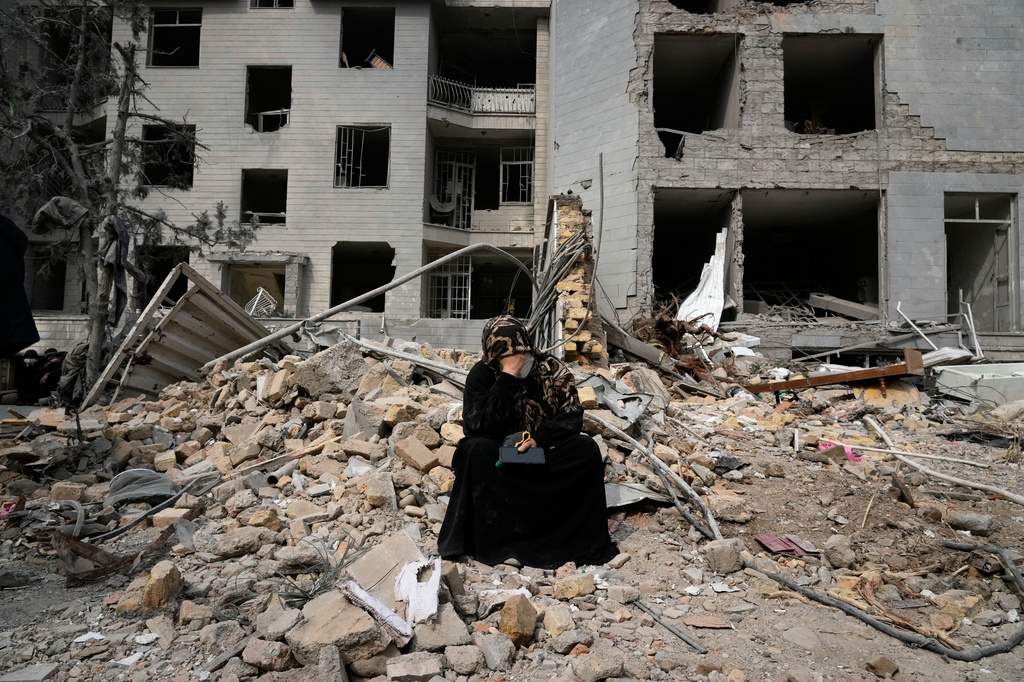  A woman sits on rubble across from a residential building damaged during the U.S.-Israeli air campaign in Tehran, Iran, March 12, 2026. 