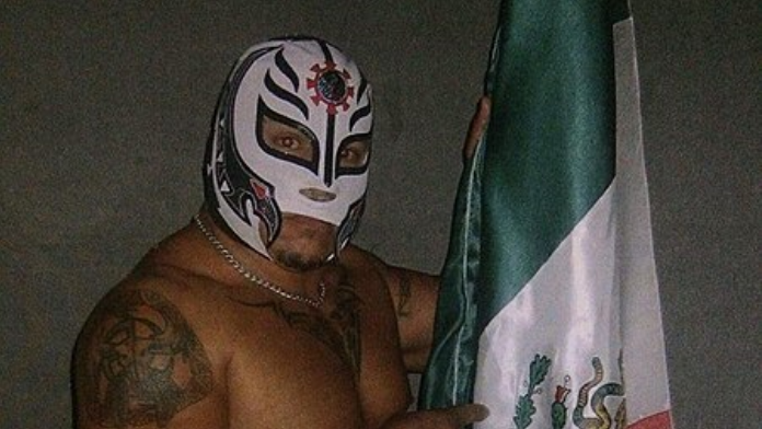 An undated promotional photo of Rey Misterio Sr. He's wearing a white mask with black detailing, standing next to a Mexican flag.