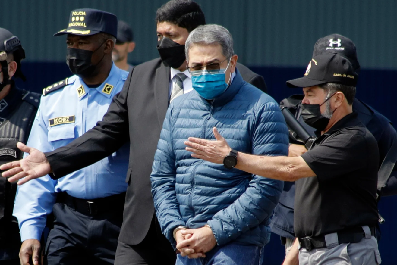 Former Honduran President Juan Orlando Hernandez, second from right, is taken in handcuffs to a waiting aircraft as he is extradited to the United States, at an Air Force base in Tegucigalpa, Honduras, April 21, 2022. 