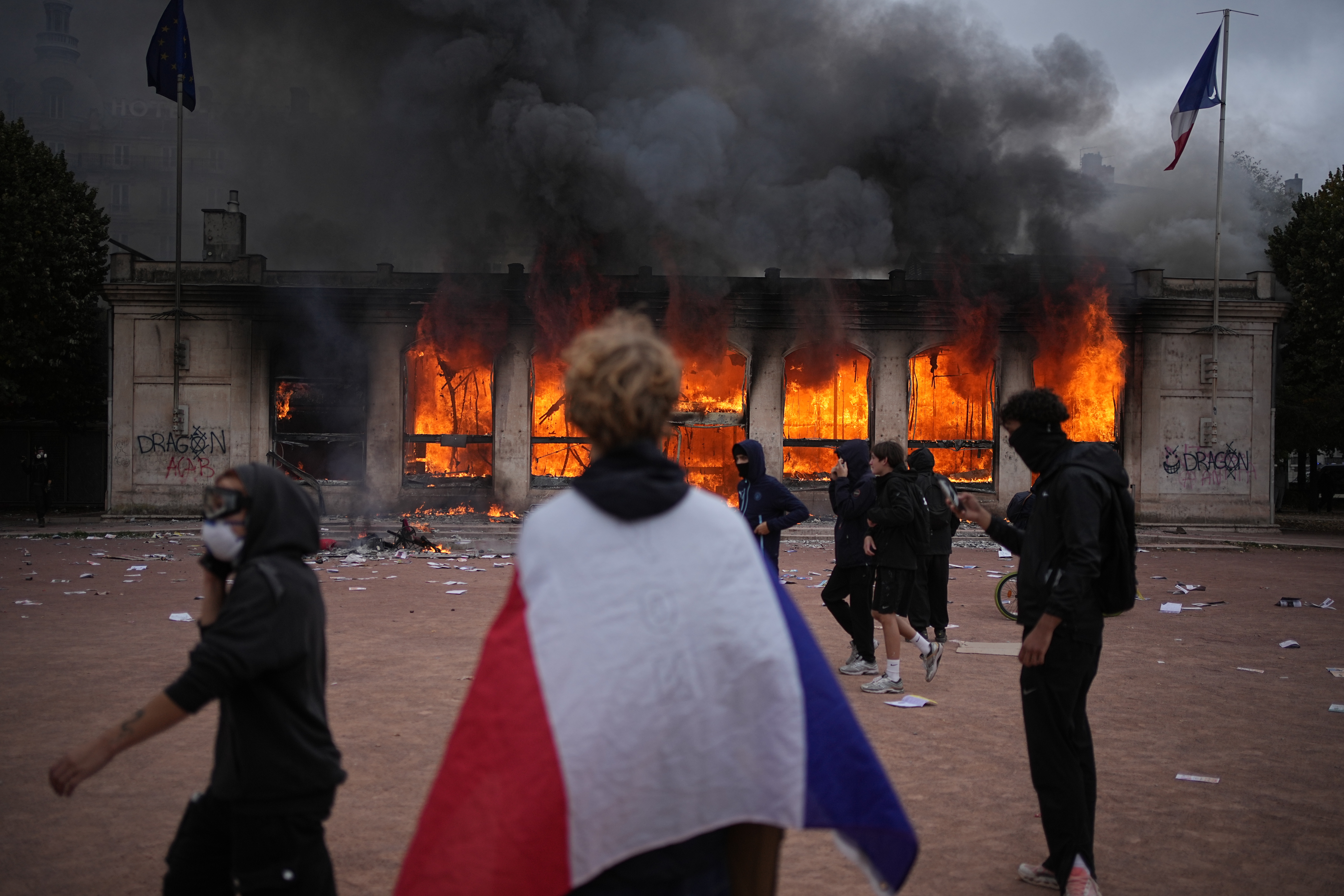 A protester wraps a French flag around them in front of the burning tourism office during a demonstration against rising living costs and in solidarity with students’ grievances in Lyon, France, Saturday, Oct. 17, 2026.