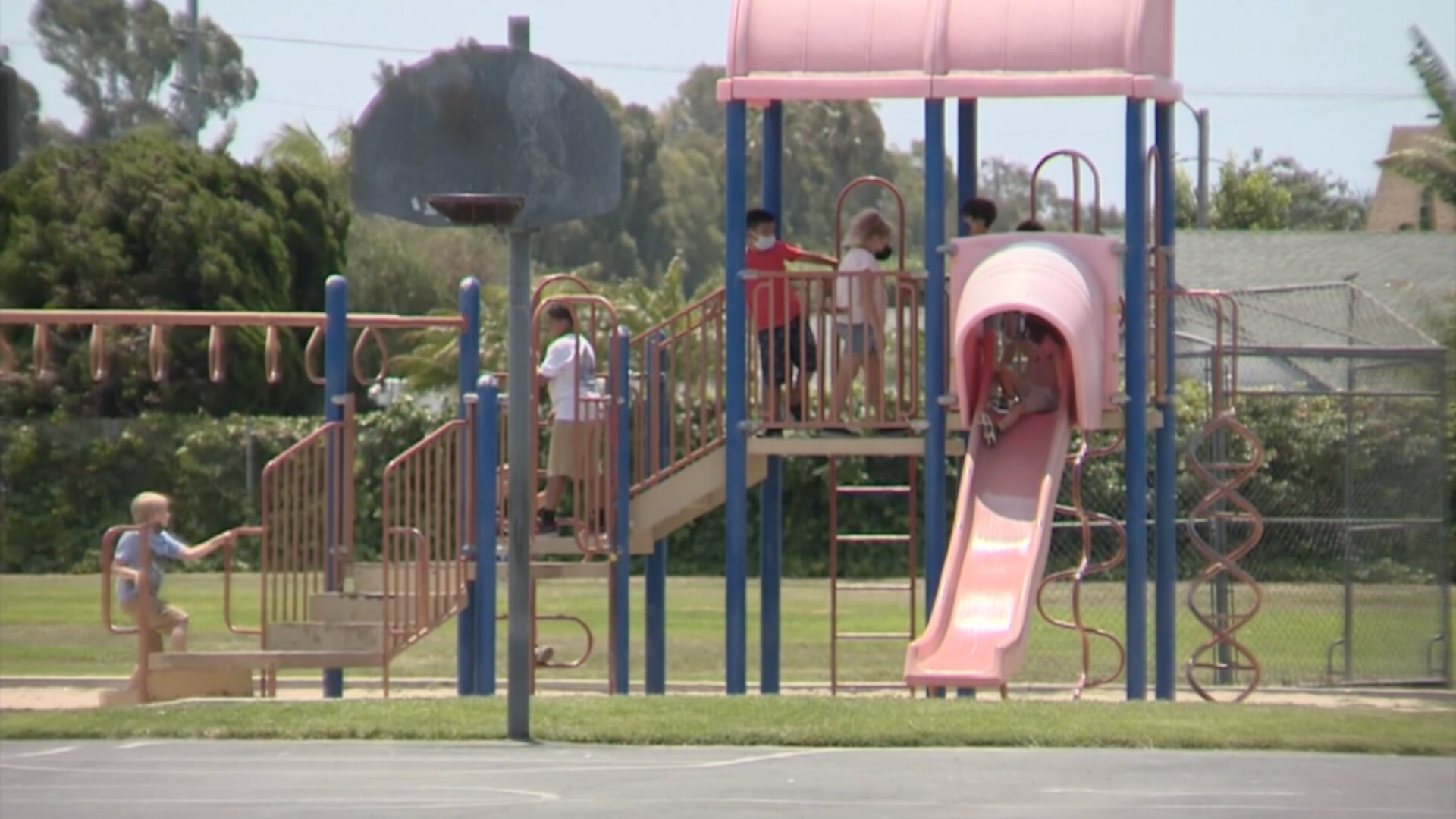 Children wearing masks play on a playground.