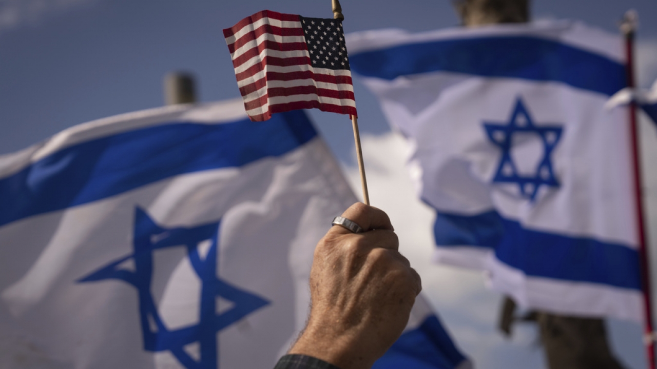 Hand holds up American flag in front of Islraeli flags