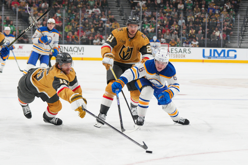 Vegas Golden Knights defenseman Noah Hanifin (15) and center Brett Howden (21) chase after the puck against Buffalo Sabres left wing Zach Benson (6) during the first period of an NHL hockey game Tuesday, March 17, 2026, in Las Vegas. (AP Photo/Candice Ward)