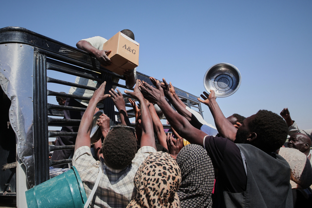 FILE.- Sudanese families displaced from El-Fasher reach out as aid workers distribute food supplies at the newly established El-Afadh camp in Al Dabbah, in Sudan's Northern State, Nov. 16, 2025.