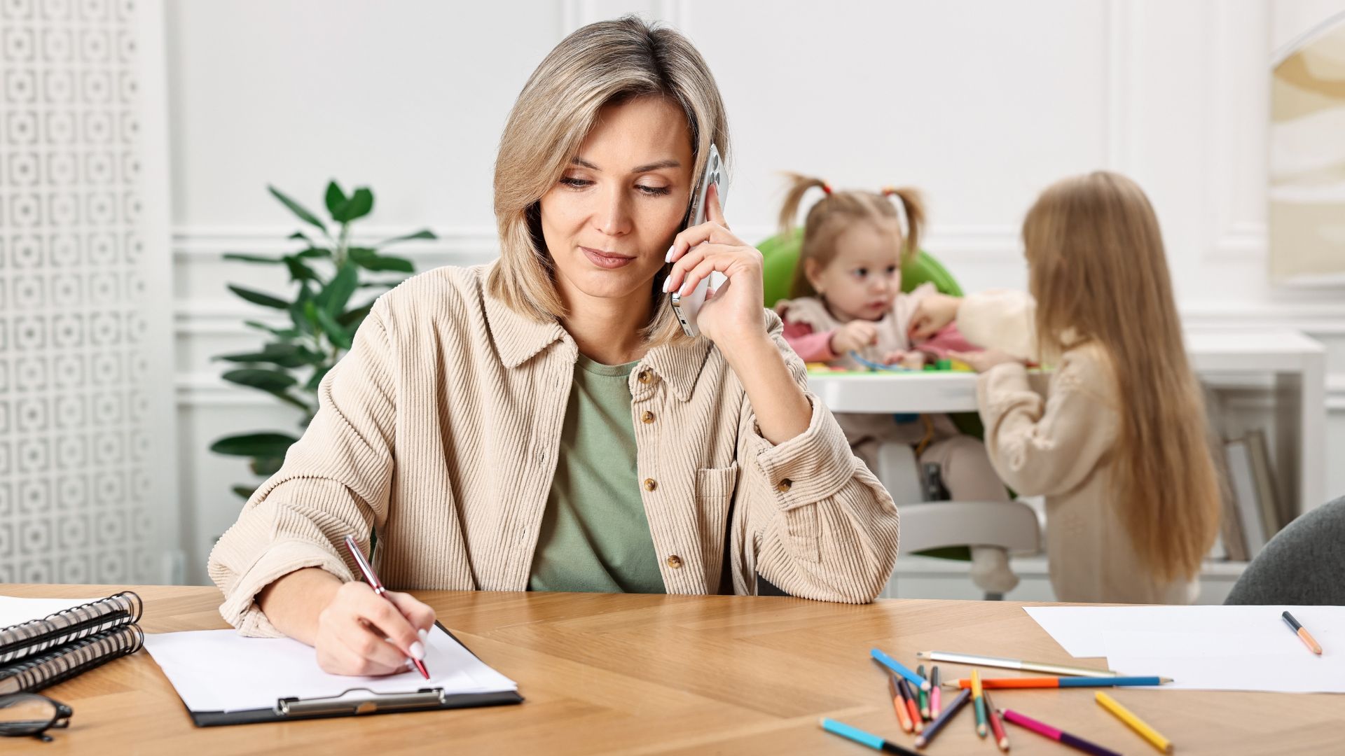 Stock image of a woman on the phone while a young child takes care of an infant in the background.