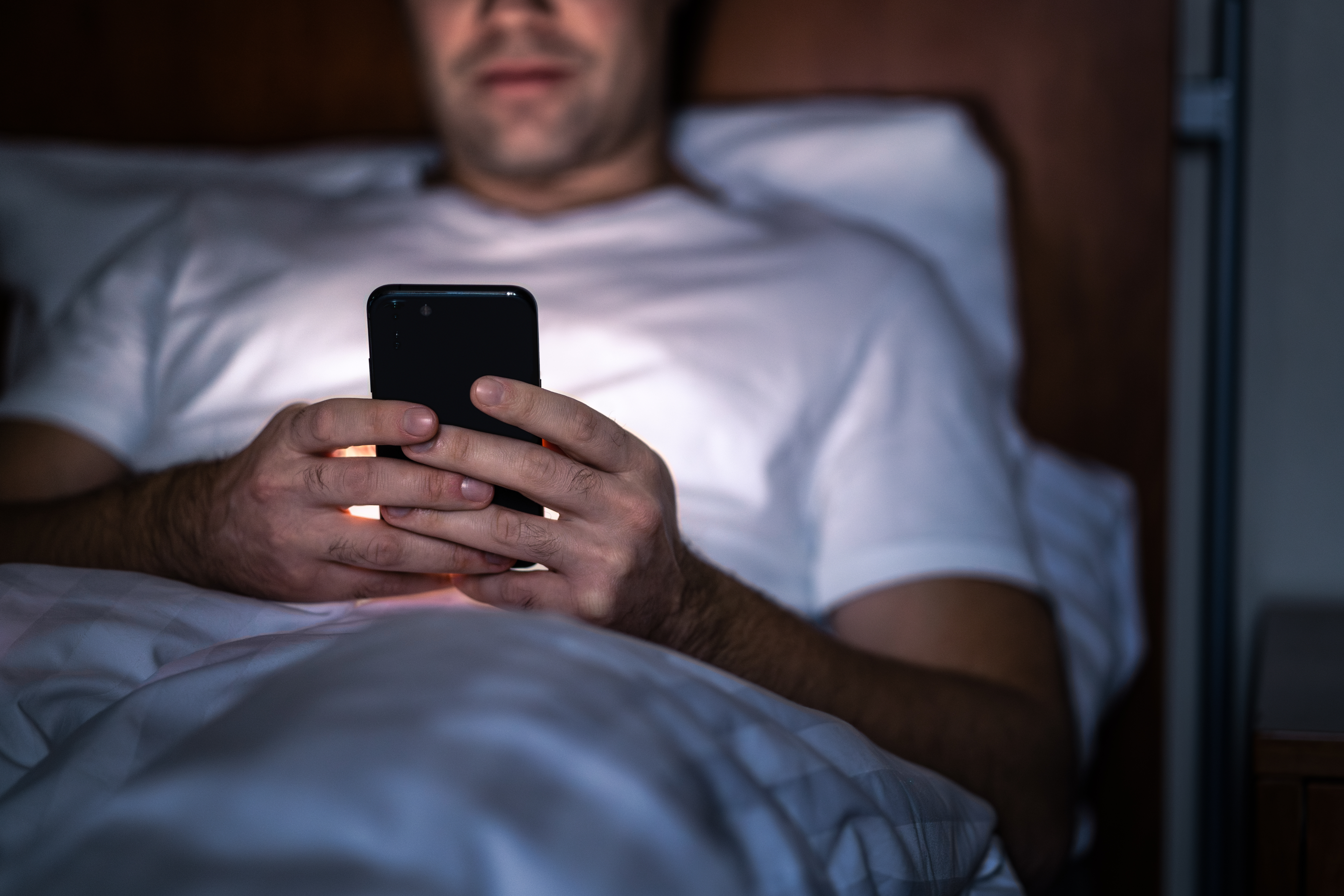 An adult using their phone in bed.