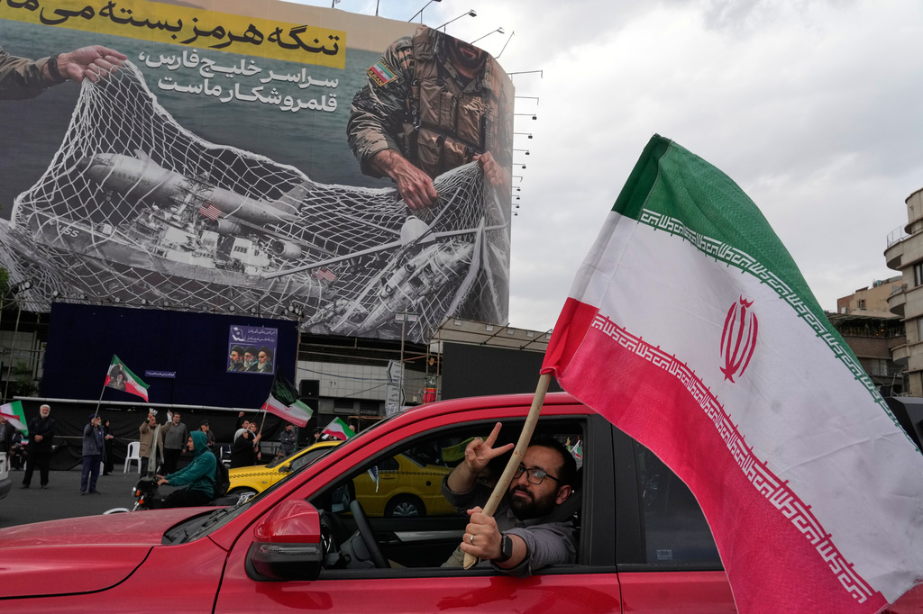 A man flashes a victory sign as he carries an Iranian flag in front of an anti-U.S. billboard depicting the American aircrafts into the Iranian armed forces fishing net with signs that read in Farsi: "The Strait of Hormuz will remain closed, The entire Persian Gulf is our hunting ground," at the Eqelab-e-Eslami, or Islamic Revolution Square in downtown Tehran, Iran, Monday, April 13, 2026. 