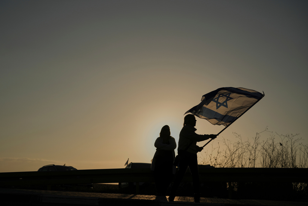 People hold Israeli flags as they gather before the release of Israeli hostages held in Gaza, outside a military base near Reim, southern Israel, on Monday, Oct. 13, 2025.