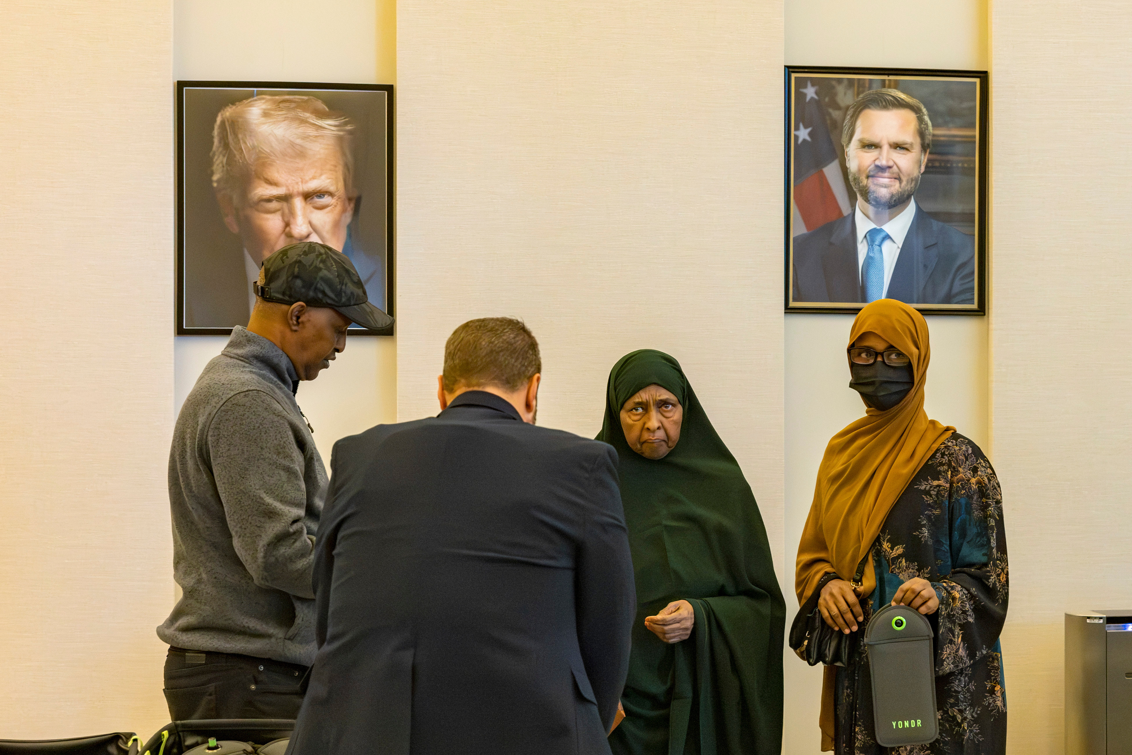Ayan, mother of Sheikhdoon Abdullahi Mohamud, right, stands with family members following her son's initial court appearance at the Warren E. Burger Federal Building on Wednesday, Oct. 7, 2026, in St. Paul, Minn., with portraits of President Donald Trump and Vice President JD Vance displayed in the background.