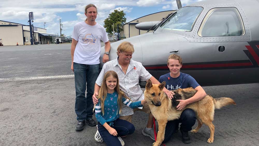 In this photo provided by the Humane Society of Broward County, kneeling from left to right, Chloe, Doug and Chase Peterson greet their long-lost German Shepherd dog Cedar on Saturday, April 20, 2019, at Fort Lauderdale Executive Airport, in Fort Lauderdale, Fla. Cedar, 2, was stolen from her home in Southwest Ranches in 2017 and located this month in Colorado. Standing is pilot Ted DuPuis. (Cherie Wachter/Humane Society of Broward County via AP)