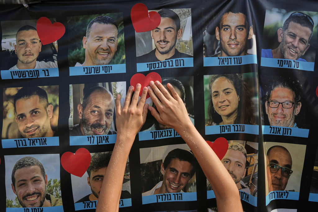A person pastes a heart-shaped sticker on a banner with pictures of Israeli hostages during a a gathering at a plaza known as hostages square in Tel Aviv, Israel, Monday, Oct. 13, 2025. 