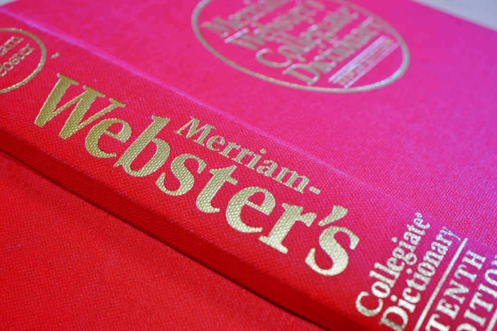 View of a Merriam Websters English dictionary with a red cover on a desk.