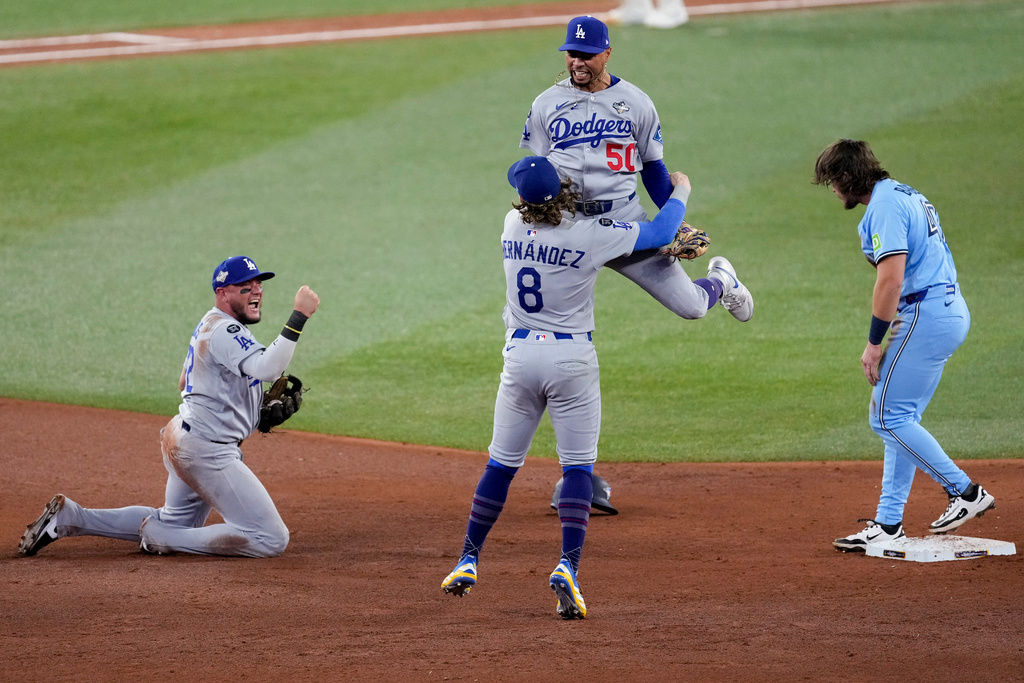 Los Angeles Dodgers' Mookie Betts (50) leaps into the arms of Kiké Hernández (8) as Miguel Rojas, left, pumps his fist after Toronto Blue Jays' Addison Barger, right, was forced out to end Game 6 of baseball's World Series, Friday, Oct. 31, 2025, in Toronto.