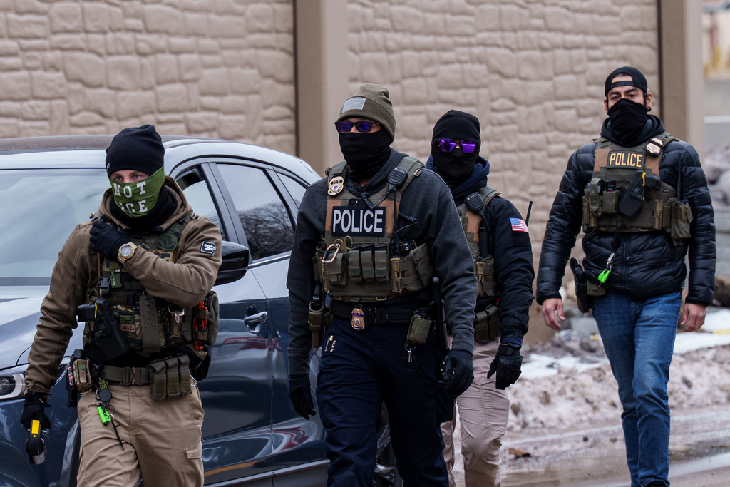 Immigration and Customs Enforcement (ICE) agents, including one wearing a 'NOT ICE' face covering, walk near their vehicles, Thursday, Jan. 15, 2026, in Richfield, Minn. 