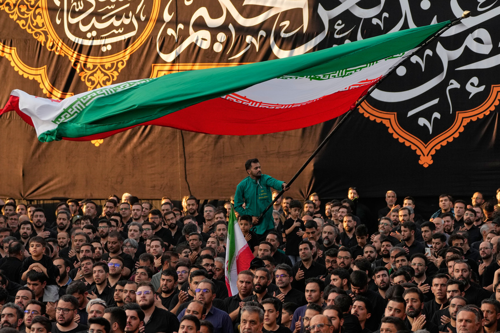 A man waves an Iranian flag as people beat their chests during a mourning ceremony in Tehran, Iran, Thursday, June 18, 2026, ahead of Ashoura, which honors the 7th-century martyrdom of the Prophet Muhammad's grandson, Hussein, who was killed in a battle in Karbala in present-day Iraq. 