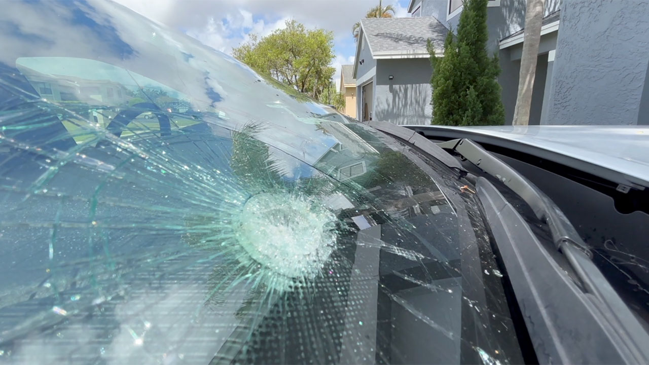 Joao Loyola, who lives along Westchester Country Club, shows off damage to his car windshield that he says came from a golf ball.