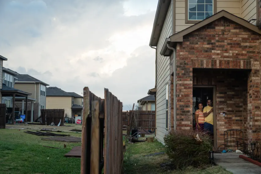 A family watches from their door as people assess damage from a tornado that struck Round Rock on March 21, 2022. As natural disasters become more severe in part due to climate change, insurance rates are rising in Texas. 