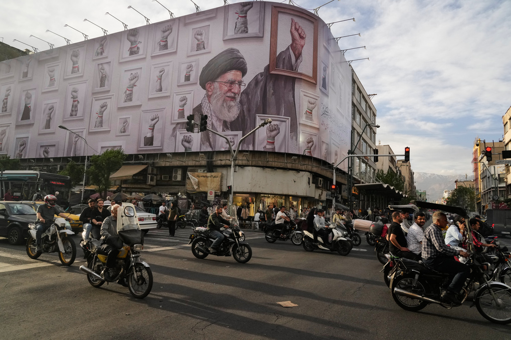 Motorbikes drive past a billboard with graphic showing the late Iranian Supreme Leader Ayatollah Ali Khamenei, who was killed in the U.S. and Israel strikes on Feb. 28, with his framed fist amongst his supporters framed fists in downtown Tehran, Iran, Wednesday, May 6, 2026.