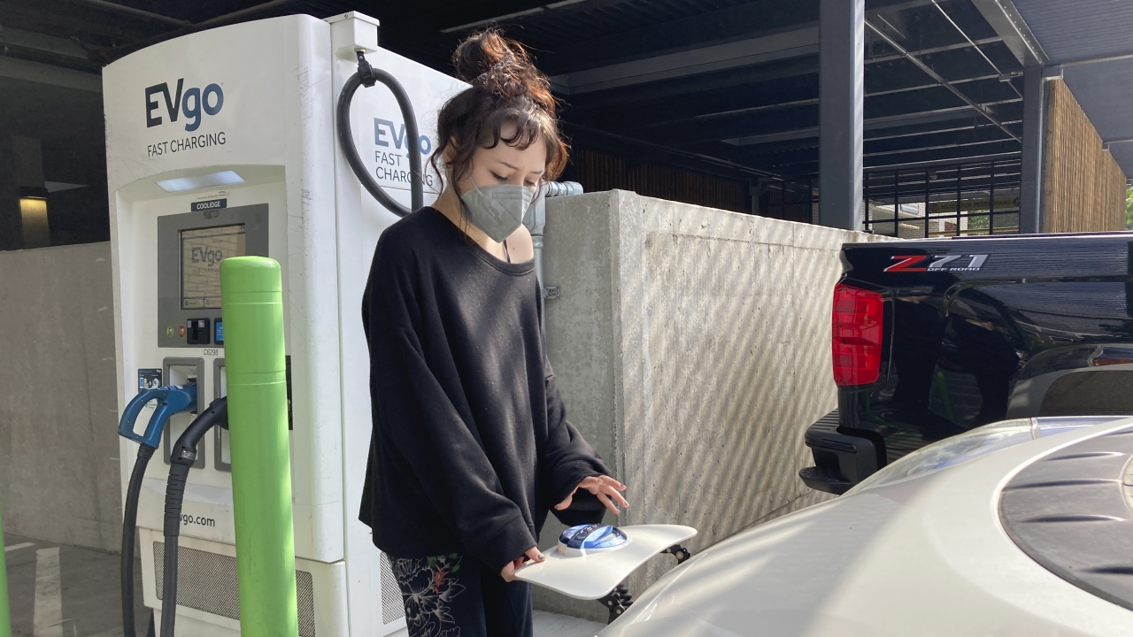 A renter who owns a used electric car, charges it at a public charging station in a grocery store parking lot