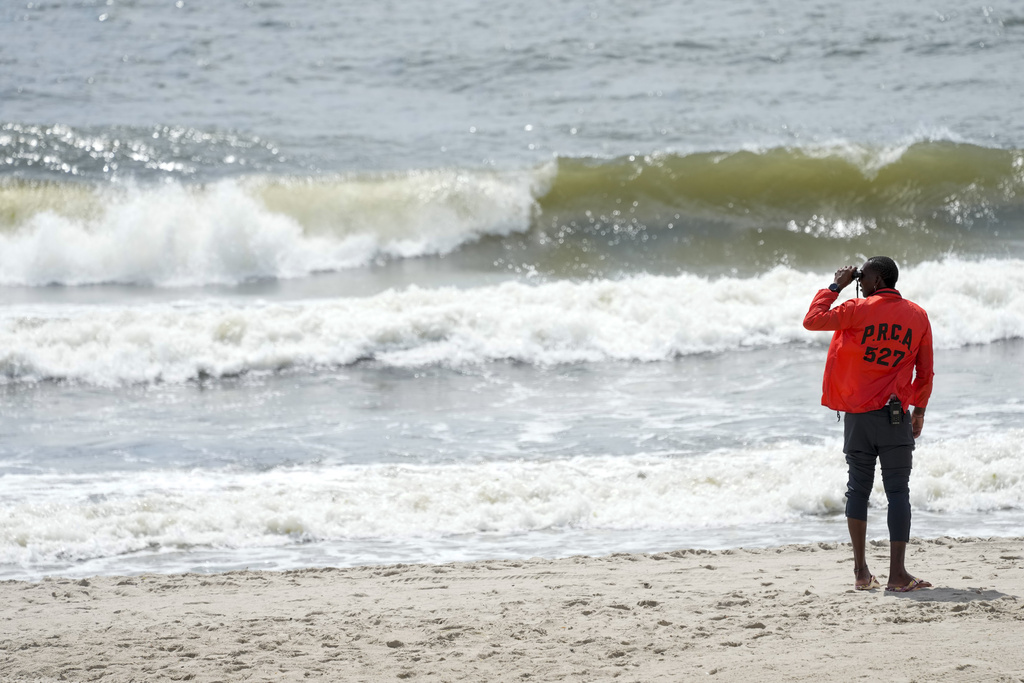 A member of the New York City Department of Parks and Recreation uses binoculars to patrol Rockaway beach, Tuesday, Aug. 8, 2023, in the Queens borough of New York.