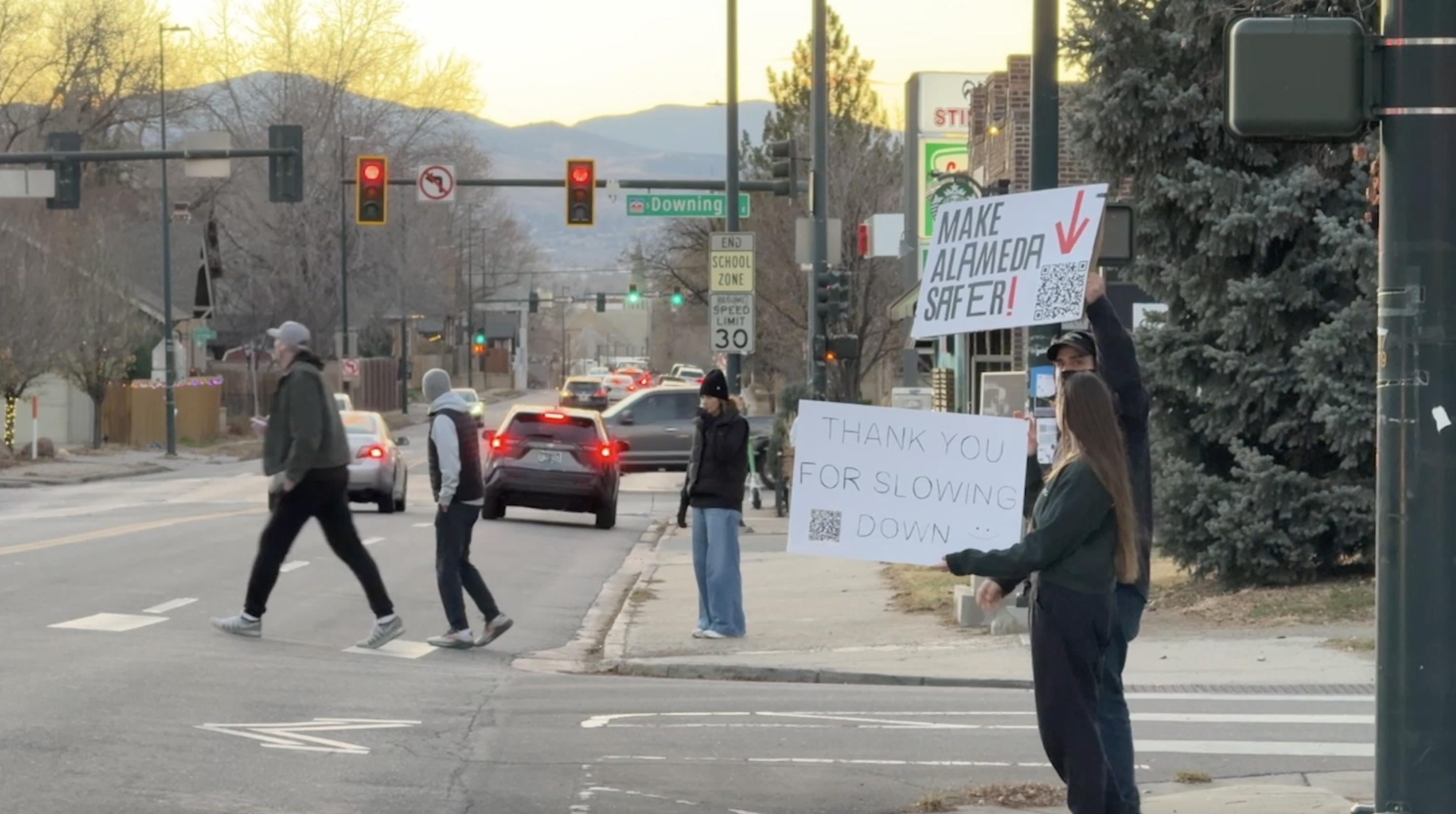 Tatianna Spector and Jamie Rooney hold up signs on Alameda Avenue, advocating for the City of Denver's original safety redesign plan.