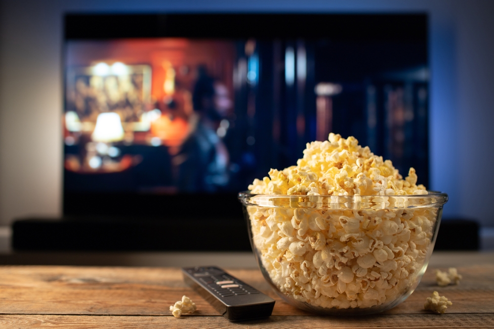 Stock image of a bowl of popcorn in front of a TV with a movie playing.