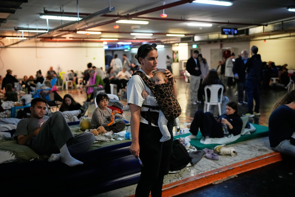 Leah Guttmann holds her son, Teddy, as other people take shelter in an underground parking garage while air-raid sirens warn of incoming missiles launched by Iran toward Tel Aviv, Israel, Sunday, March 1, 2026.