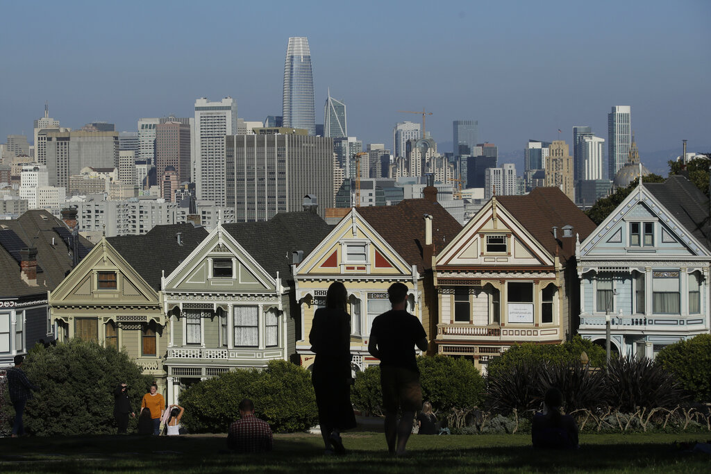 FILE - In this Feb. 26, 2020, file photo, visitors look toward the "Painted Ladies," a row of historical Victorian homes, in front of the San Francisco skyline from Alamo Square Park in San Francisco.