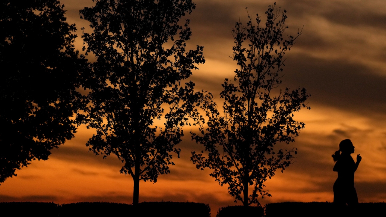 A woman is silhouetted against the sky at sunset as she runs in a park