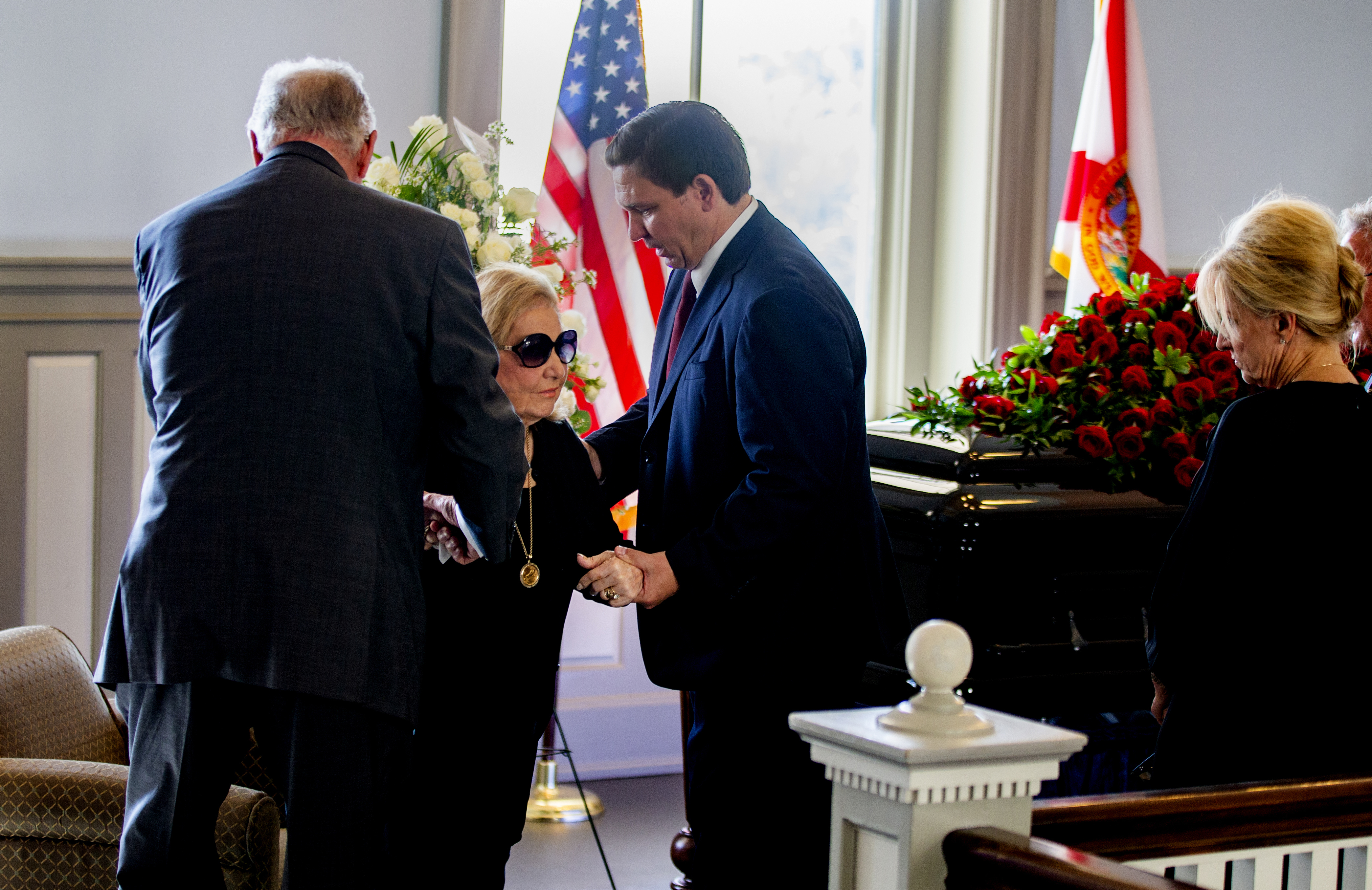 Gov. Ron DeSantis helps Ann Bowden into her seat as husband lies in honor at old Florida Capitol, Aug. 13, 2021