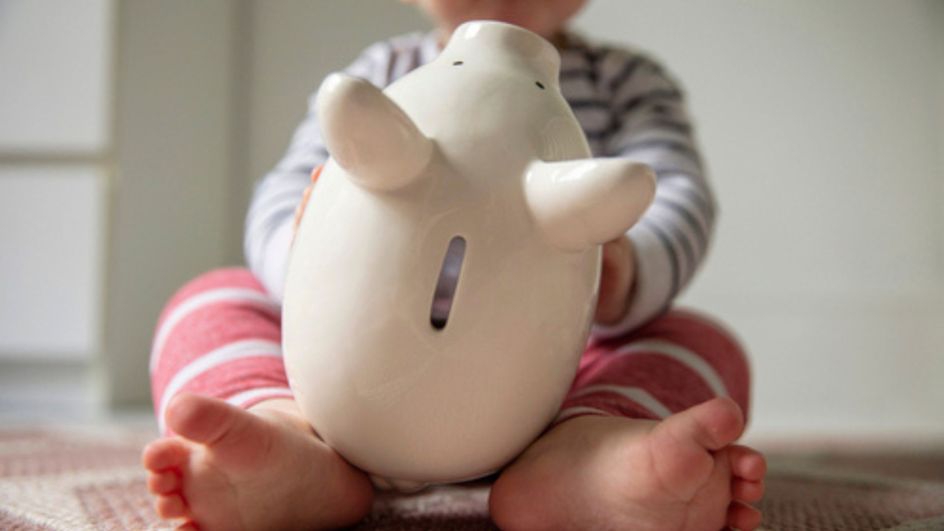 Stock image of a baby holding a piggy bank.