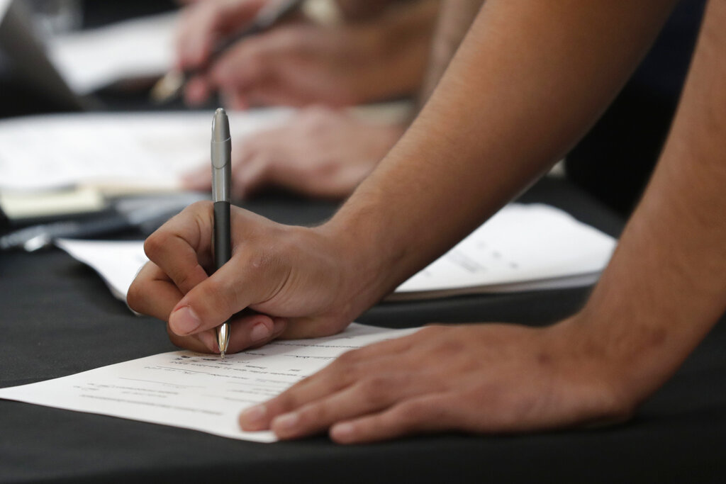 FILE - In this Oct. 1, 2019, file photo job seekers fill out applications during a job fair at Dolphin Mall in Miami. 