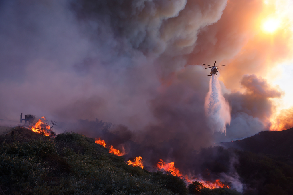 Water is dropped by helicopter on the advancing Palisades Fire in the Pacific Palisades neighborhood of Los Angeles, Tuesday, Jan. 7, 2025. 