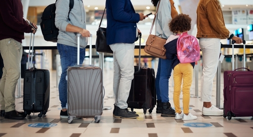 People stand in line with their luggage at an airport.