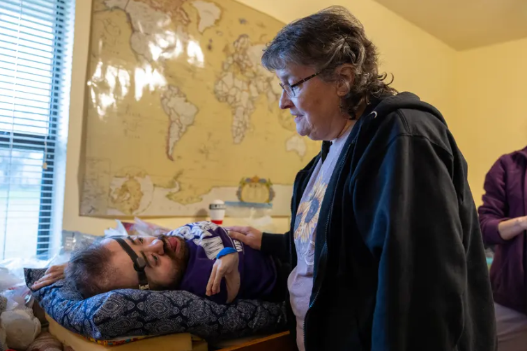 Debbie Wiederhold talks with her 31-year-old son Daniel at their home in Hutto on Feb. 29, 2024. Though Daniel was born with a rare brittle bone disorder, he lives an active life with support from state services.