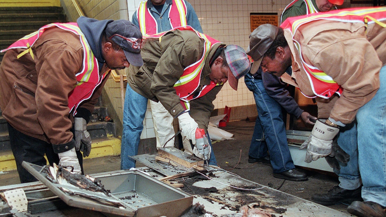Transit workers dismantle the charred inner wall of a token booth
