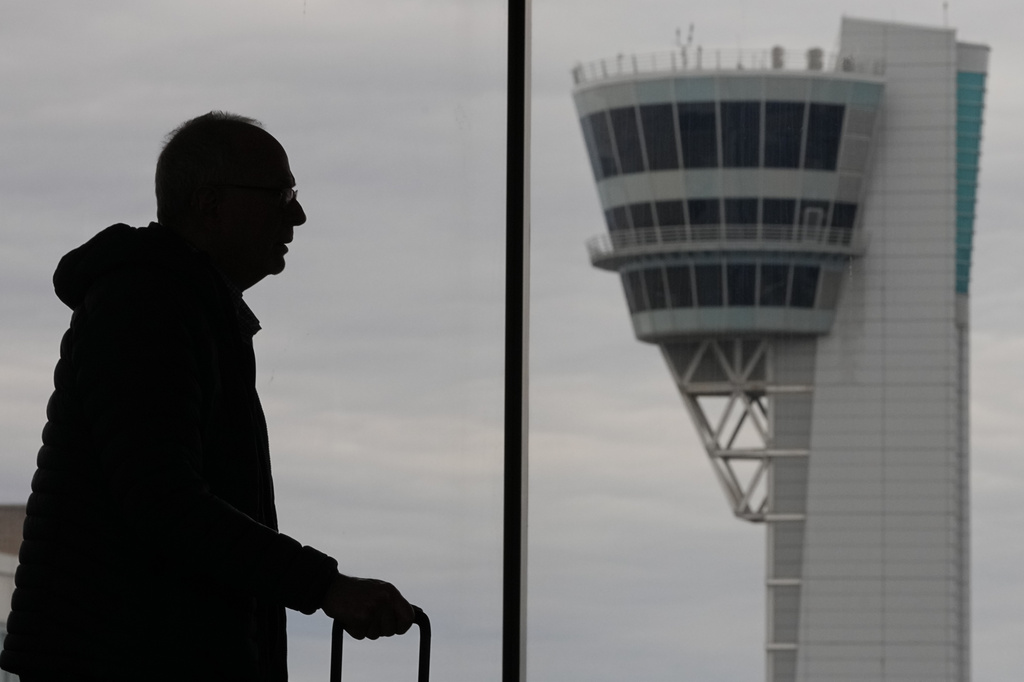 A traveler moves in view of an air traffic control tower at Philadelphia International Airport in Philadelphia, Friday, March 27, 2026.
