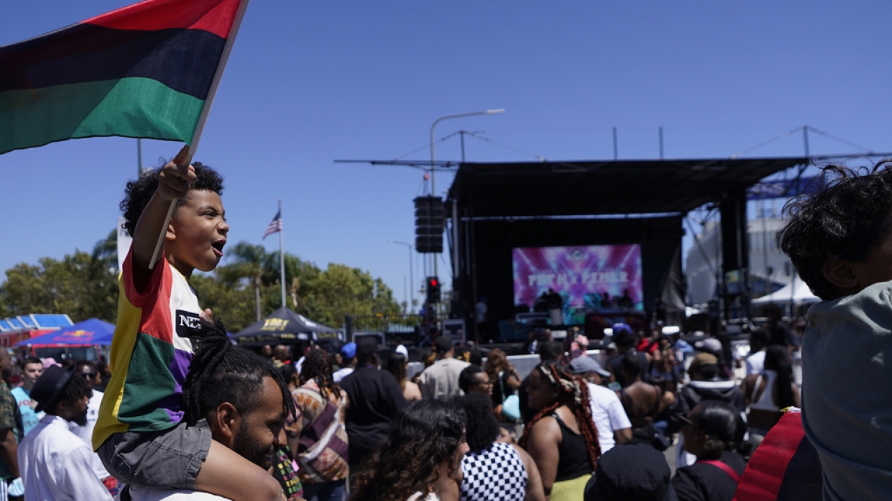 A boy sits on his father's shoulders holding a Pan-African flag during a Juneteenth celebration