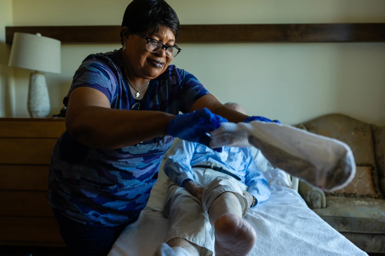 Jackie Conteh, an advanced care partner originally from Sierra Leone, helps Donald Goodness, 92, put on fresh socks in his apartment at Goodwin House Alexandria, Thursday, Oct. 16, 2025, in Alexandria, Va.