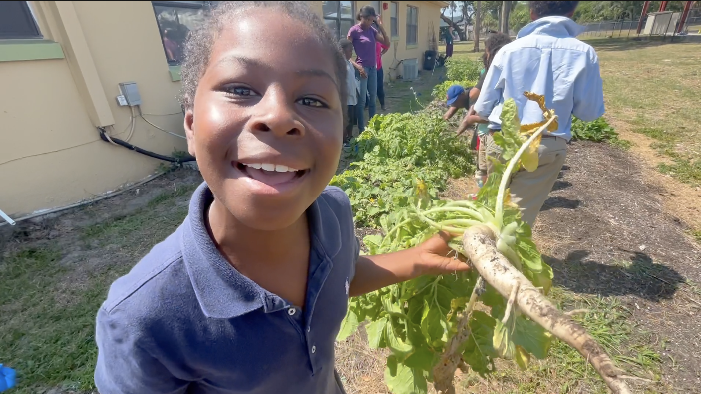 An elementary student holds a large vegetable during an after-school program with USF anthropologists