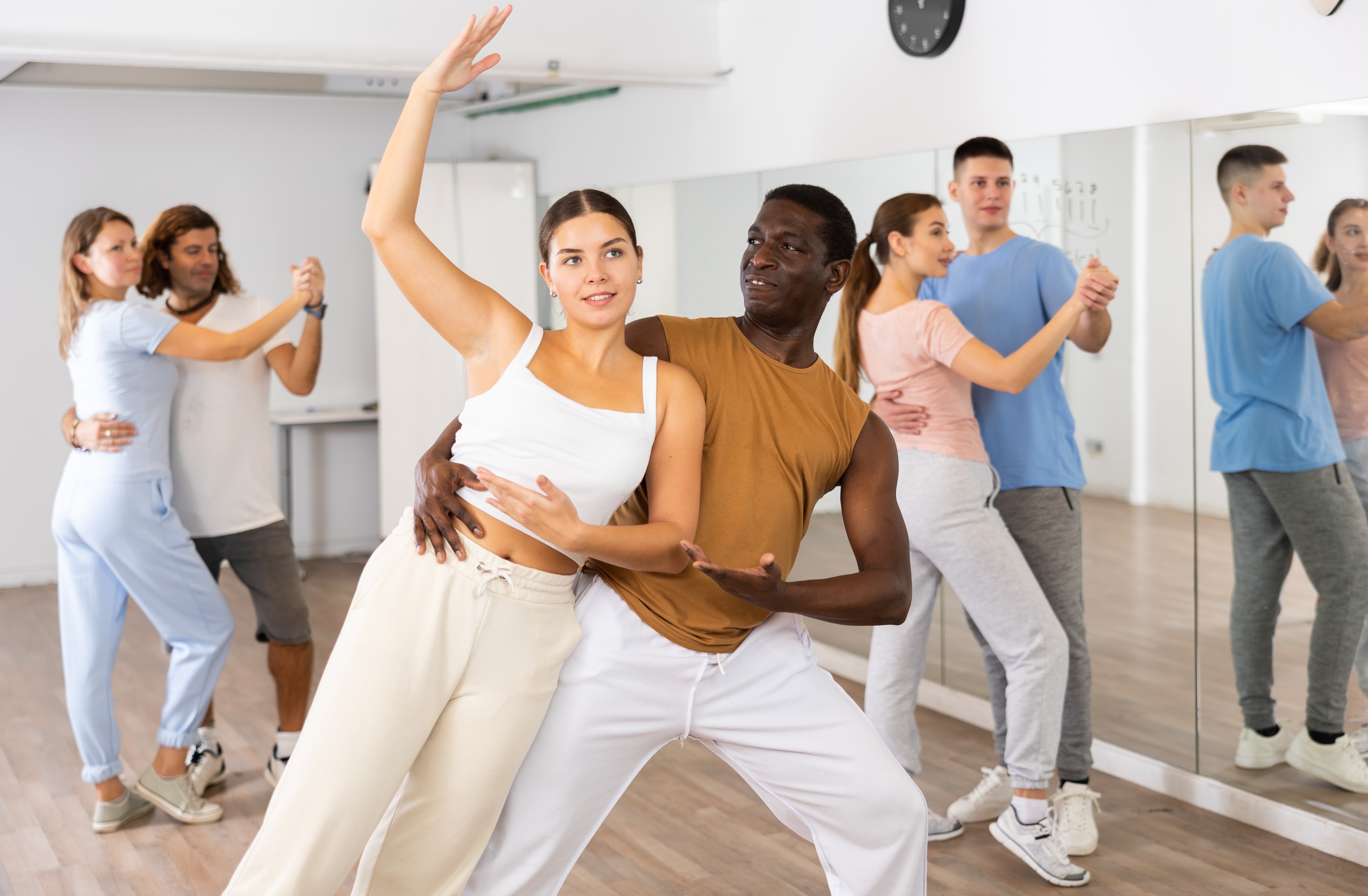 Group of excited young adult people dancing dynamic moves in pairs during lesson in dance class