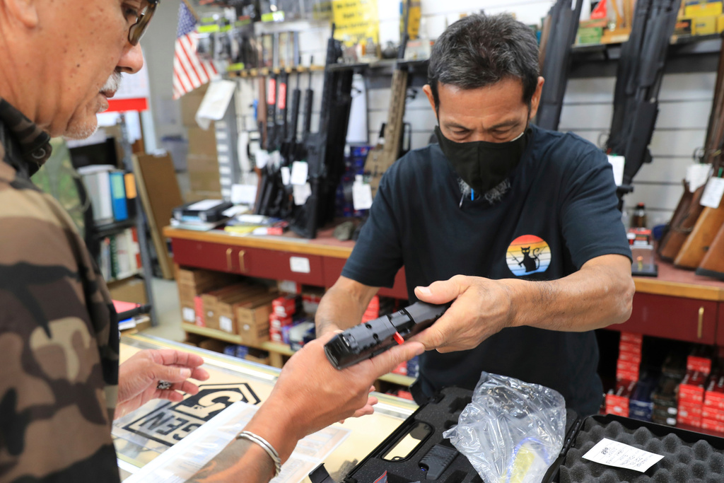 A clerk hands a gun to a customer inside a gun shop in Honolulu, June, 23, 2022. 