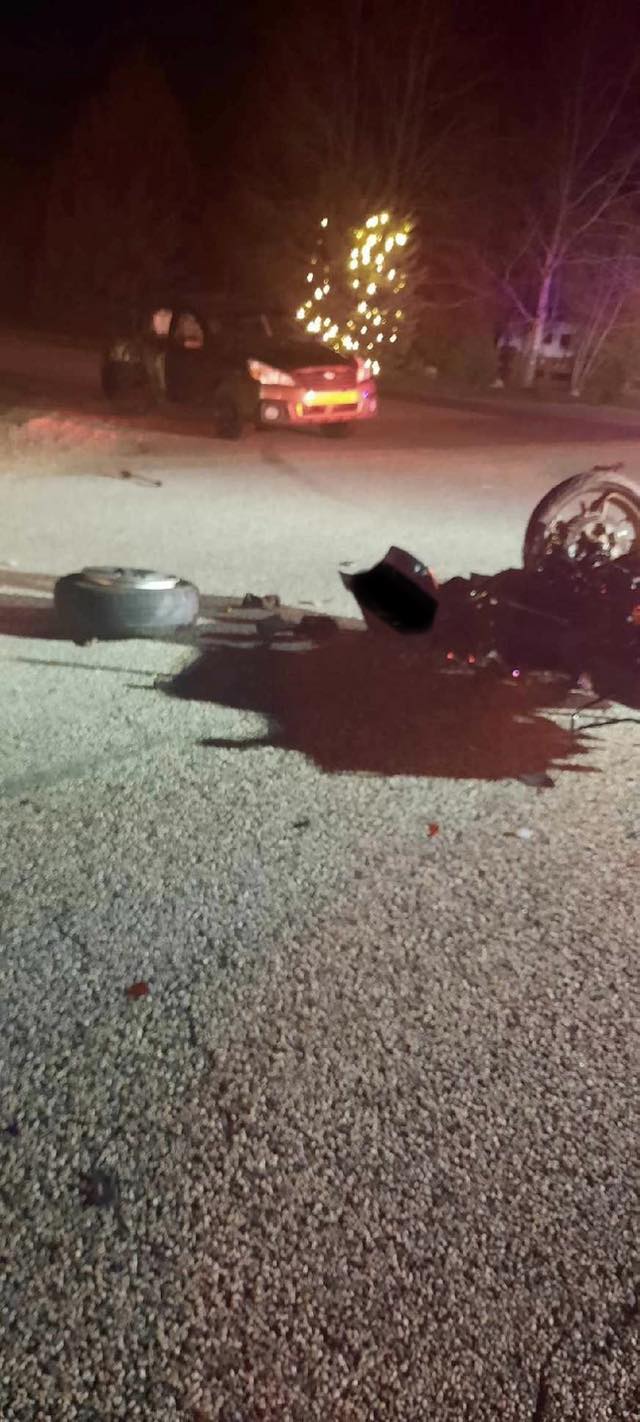 An image from the accident scene released by Mountain Green Fire Protection District. It's nighttime. In the foreground, we see the damaged motorcycle and what appears to be a puddle of fuel next to it. The car it collided with is in the background.